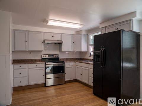 A black refrigerator is in the corner of a kitchen with white cabinets and a stainless steel oven.