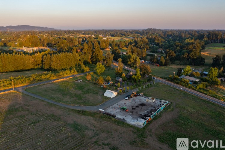 An aerial view of a construction site in the middle of a field with a house and trees in the background.