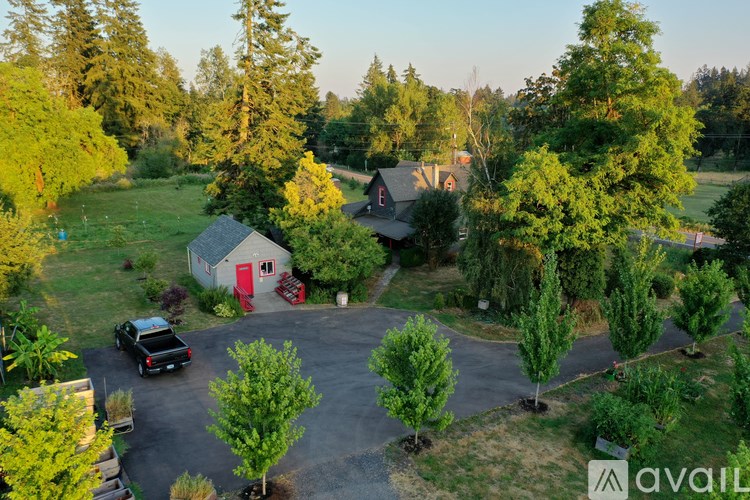 A house with a red door is surrounded by trees and a black car is parked in the driveway.