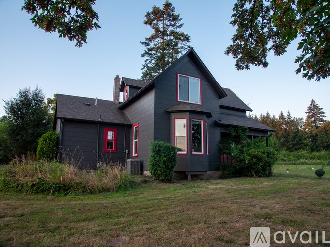 A house with a red door and a chimney is surrounded by greenery.
