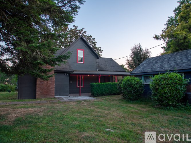 A house with a grey roof and a red door is surrounded by greenery.