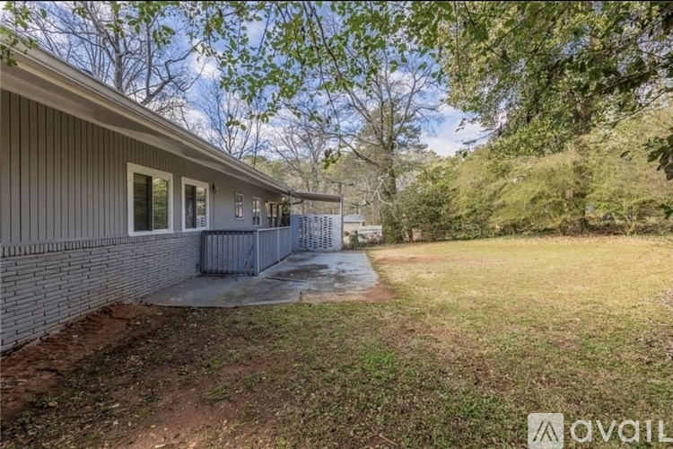 A house with a grey siding and a brown roof is surrounded by trees and has a grassy area in front.