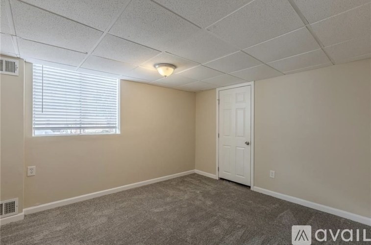 A room with a carpeted floor, a window with blinds, a door, and a ceiling with lights.