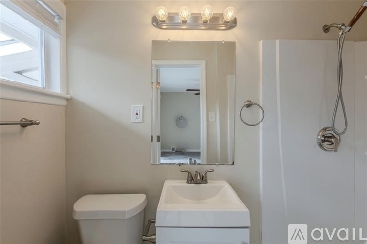 A bathroom with a toilet, sink, mirror, and shower.