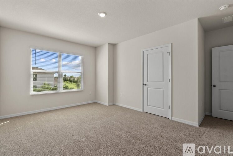 A room with a window showing a view of a house and trees outside.