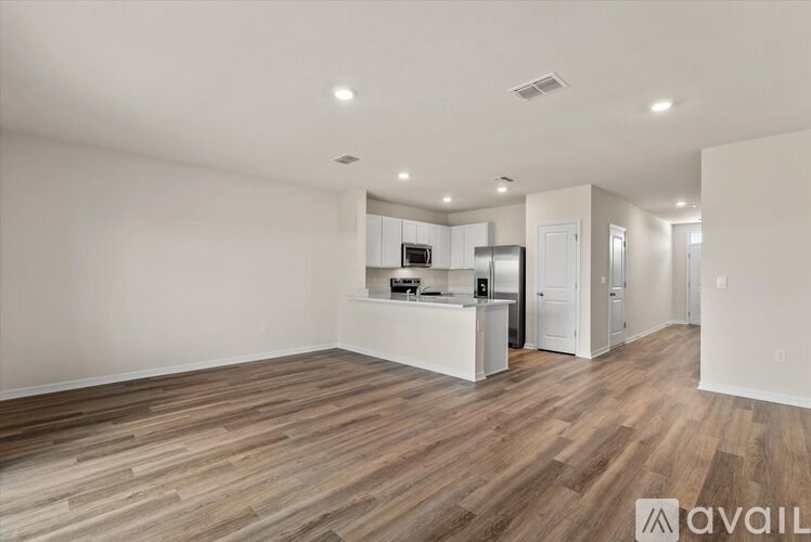 A spacious kitchen with wooden flooring and white walls.