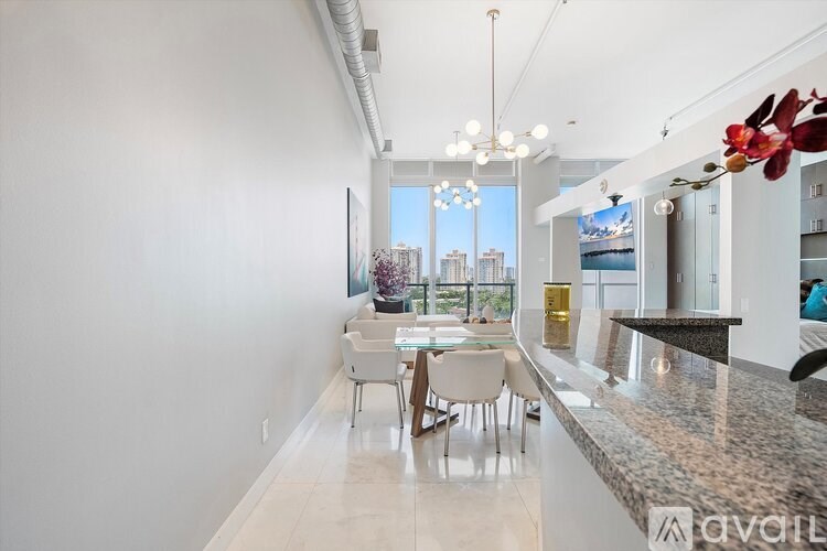 A modern kitchen with a dining table and chairs in the foreground and a city view through the window.