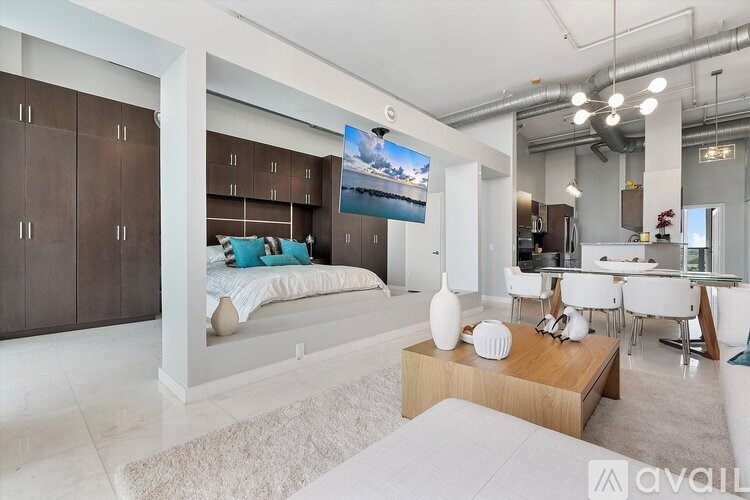 A modern bedroom with a large bed, a wooden coffee table, and a dining area in the background.