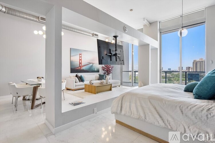 A bedroom with a large bed, a desk with a chair, and a view of the city through the window.