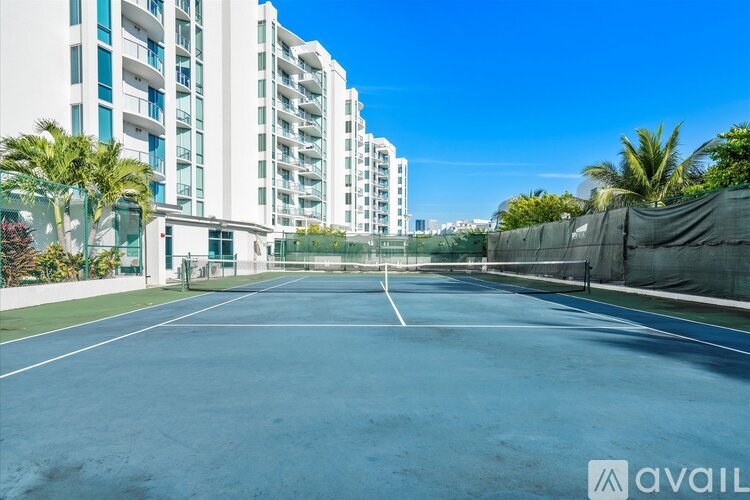 A tennis court is surrounded by apartment buildings.