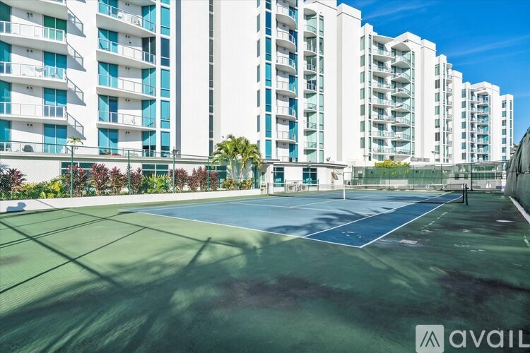 A tennis court is located in front of a row of apartment buildings.