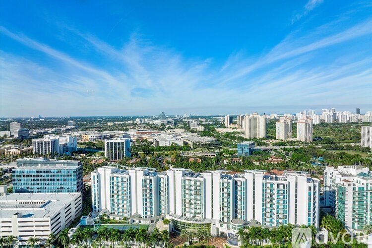 A cityscape with tall buildings and palm trees under a clear sky.