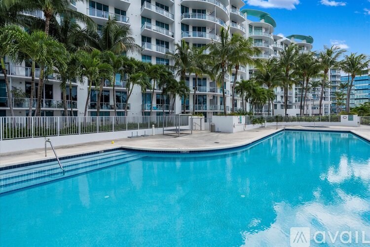 A swimming pool in front of a white building surrounded by palm trees.
