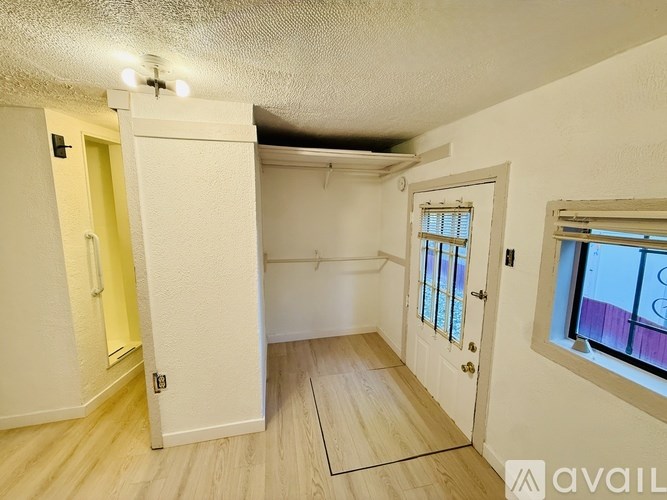 A room with a white door, a window with a purple curtain, and a wooden floor.