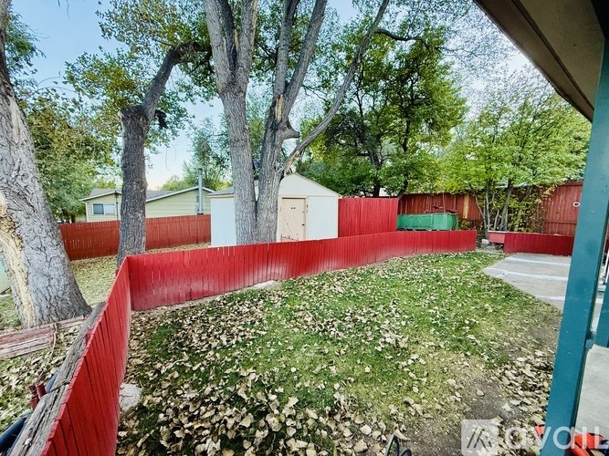 A red fence surrounds a yard with a tree and a house in the background.