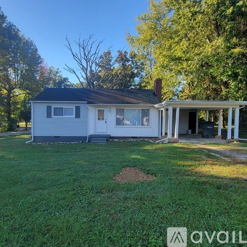 A house with a white and grey exterior is surrounded by green grass and trees.