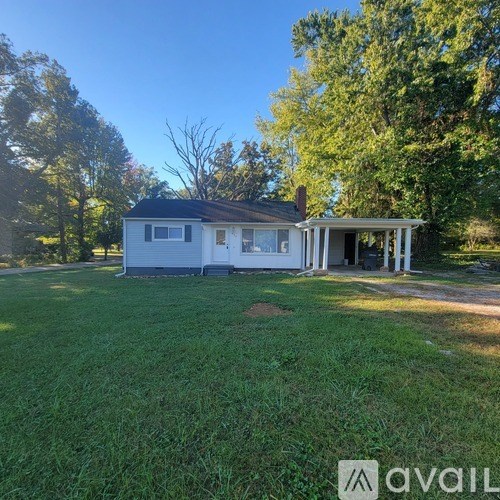A house with a white exterior and a black roof is surrounded by green grass and trees.