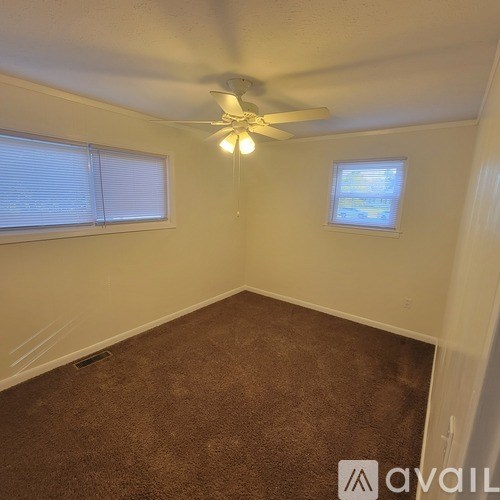 A room with a ceiling fan and two windows.