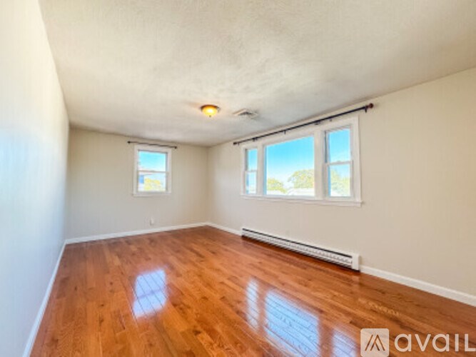 A room with wooden floors and white walls has a window with a view of the sky.