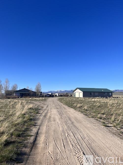 A dirt road leads to a green barn and a black building.