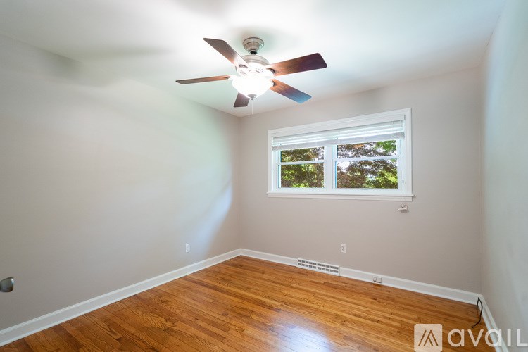 A room with a ceiling fan and a window showing greenery outside.