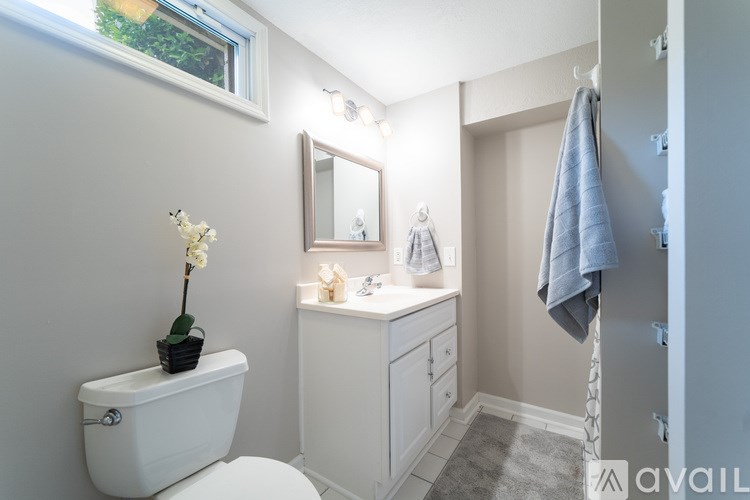 A white bathroom with a toilet, sink, mirror, and a towel hanging on the door.