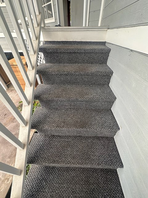 A staircase with a grey carpeted runner and a white wall on the side.