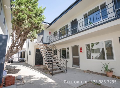 A white building with a tree in front and a staircase leading to the entrance.