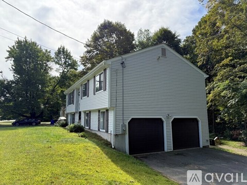 A two-story house with a garage is surrounded by greenery.