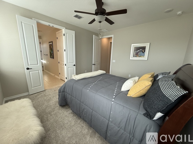 A bedroom with a bed, a ceiling fan, and a doorway leading to another room.