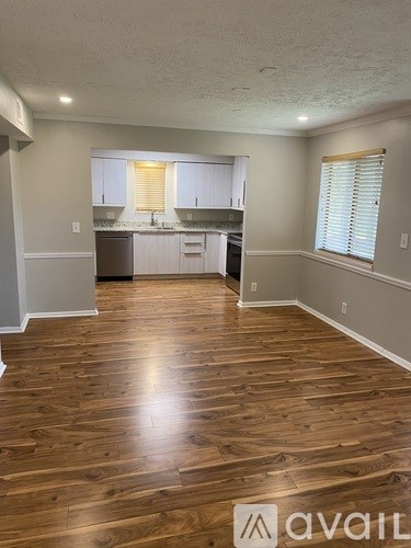 A room with wooden flooring and a kitchen area in the background.
