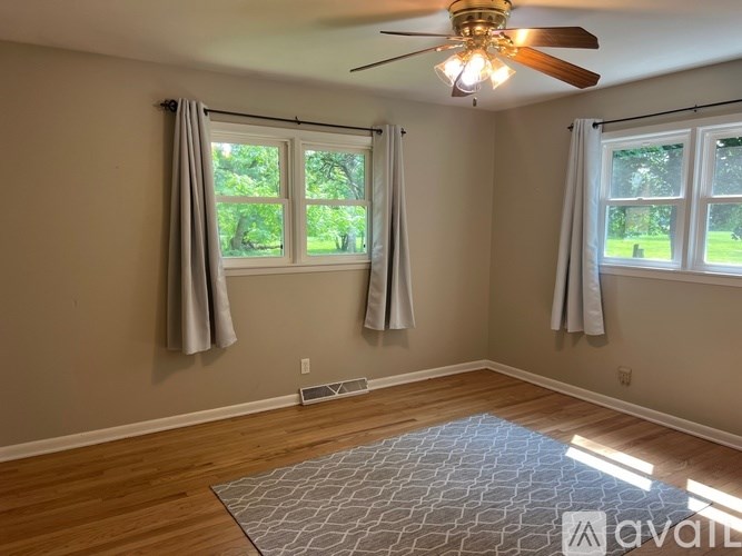 A room with a ceiling fan and two windows with curtains.