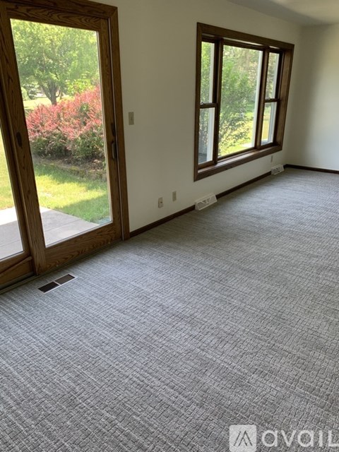 A room with a carpeted floor and a window overlooking a garden.