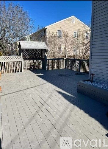 A wooden deck with a pergola and a building in the background.