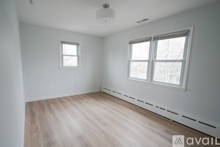 A room with wooden flooring and two windows.