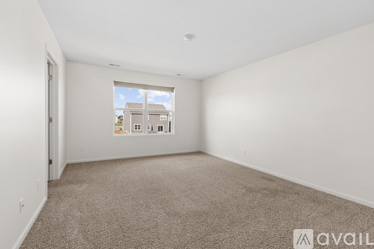 A spacious room with a carpeted floor and a window showing a view of houses.