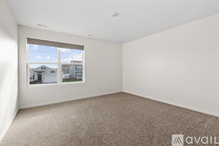 A room with a carpeted floor and a window showing a view of houses outside.