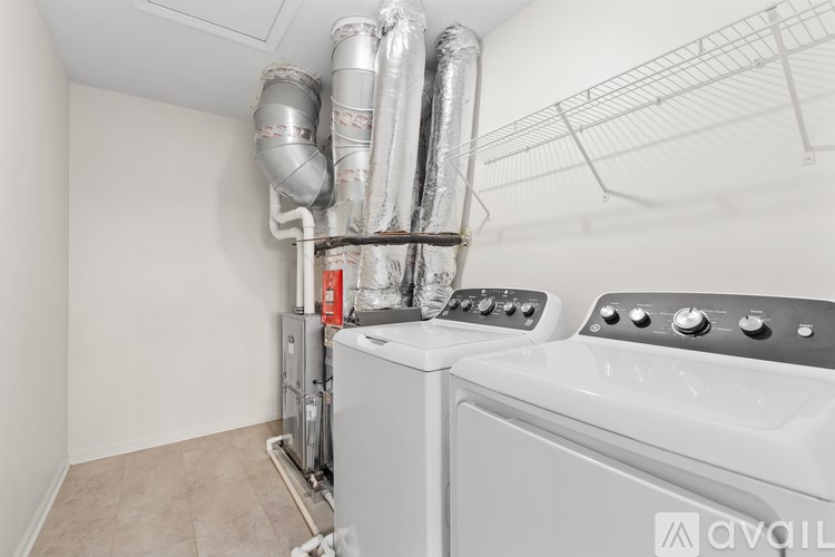 A white washing machine in a laundry room with pipes and a dryer vent.