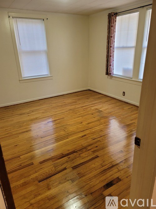 A room with wooden flooring and two windows.