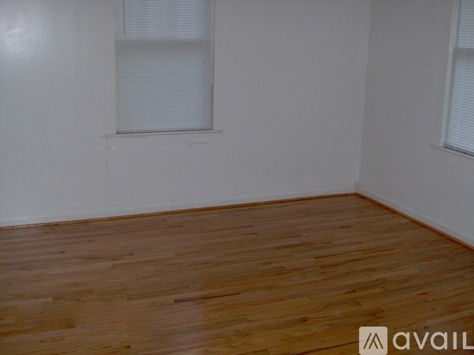 A room with wooden flooring and two windows.