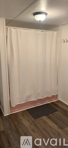A bathroom with a white shower curtain and wooden flooring.