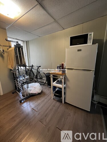 A room with a white refrigerator, a microwave on top of it, a wooden table, a chair, a bicycle, and a treadmill.