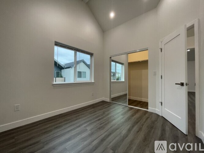 A room with a large window and wooden flooring is available for rent.