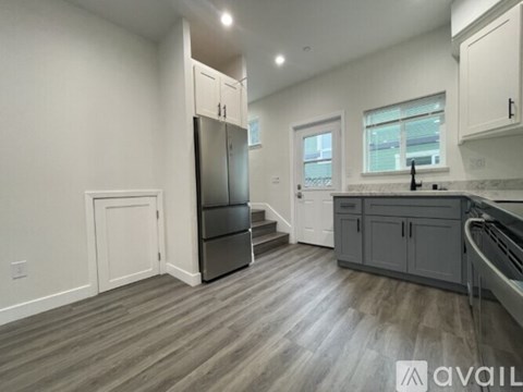 A kitchen with a refrigerator, cabinets, and a staircase.