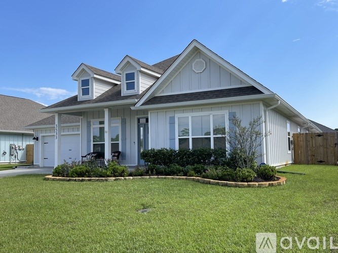 A house with a white exterior and a brown roof is surrounded by a well-manicured lawn.