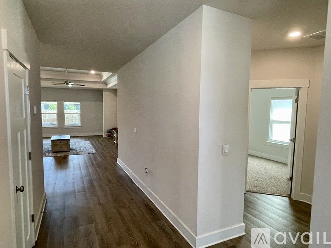 A room with white walls and wooden flooring, with a door on the left and a window on the right.