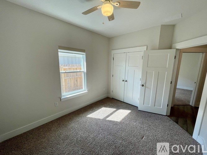 A room with a carpeted floor, a ceiling fan, and a window with a view of a wooden fence.