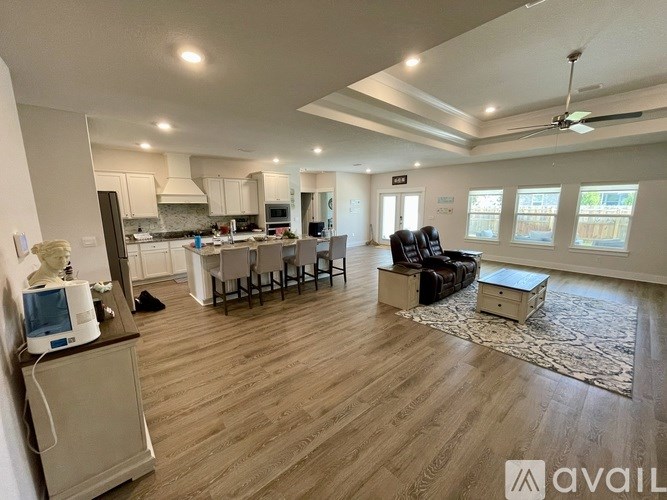A spacious living room with hardwood floors and a kitchen area in the background.