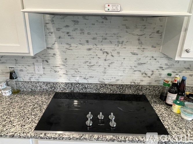 A black induction cooktop with four burners is on a granite countertop.