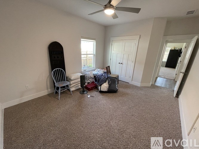 A room with a carpet floor, a ceiling fan, and a chair with a snowboard leaning against the wall.
